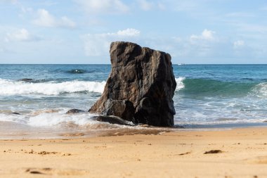A wave breaks about a rock during a curtain on the sea. Farol da Barra beach, Salvador, Brazil.