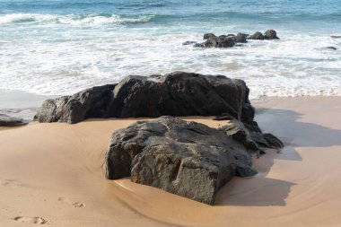 A wave breaks about a rock during a curtain on the sea. Farol da Barra beach, Salvador, Brazil.