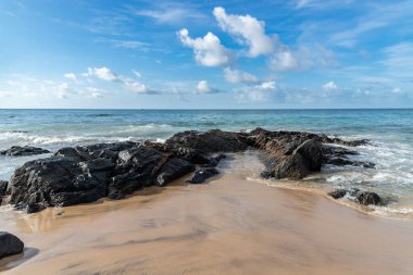 A wave breaks about a rock during a curtain on the sea. Farol da Barra beach, Salvador, Brazil.