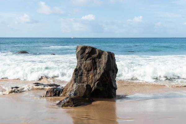 A wave breaks about a rock during a curtain on the sea. Farol da Barra beach, Salvador, Brazil.