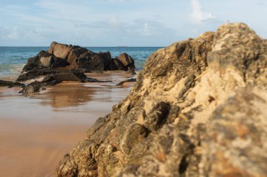 A wave breaks about a rock during a curtain on the sea. Farol da Barra beach, Salvador, Brazil.