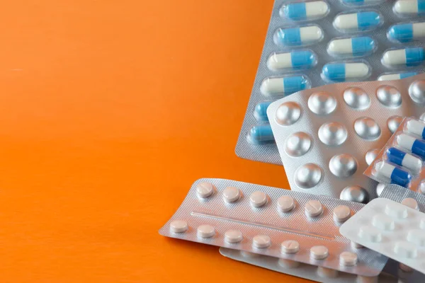 Carton of different pills, medicines, pills stacked on orange background. Medical supplies.