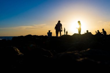 Silhouette of people on top of the beach rocks. Late afternoon in Salvador, Bahia, Brazil.