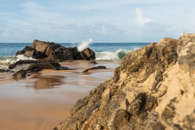 A wave breaks about a rock during a curtain on the sea. Farol da Barra beach, Salvador, Brazil.