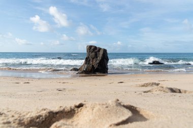 A wave breaks about a rock during a curtain on the sea. Farol da Barra beach, Salvador, Brazil.