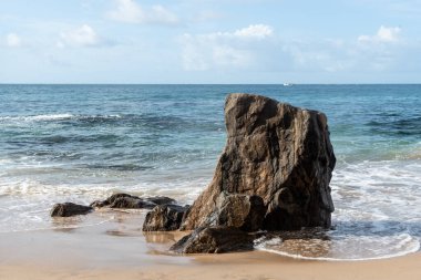 A wave breaks about a rock during a curtain on the sea. Farol da Barra beach, Salvador, Brazil.