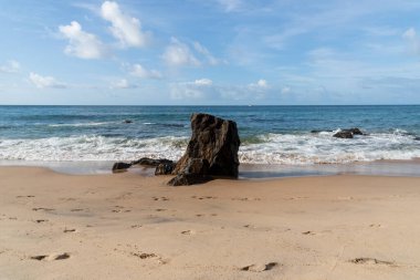 A wave breaks about a rock during a curtain on the sea. Farol da Barra beach, Salvador, Brazil.
