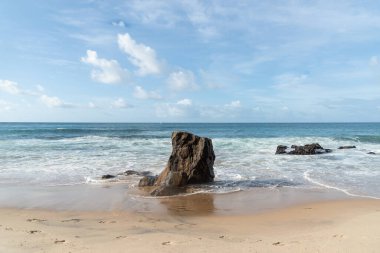 A wave breaks about a rock during a curtain on the sea. Farol da Barra beach, Salvador, Brazil.