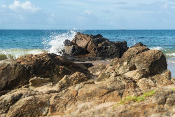 A wave breaks about a rock during a curtain on the sea. Farol da Barra beach, Salvador, Brazil.