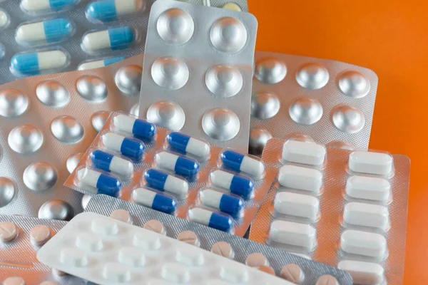 Carton of different pills, medicines, pills stacked on orange background. Medical supplies.
