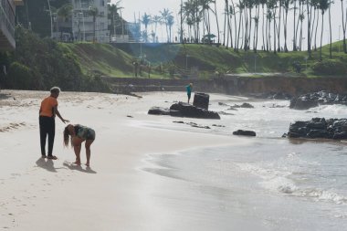 Image of people on Farol da Barra beach, against coconut trees in silhouette in the background. Salvador, Brazil.