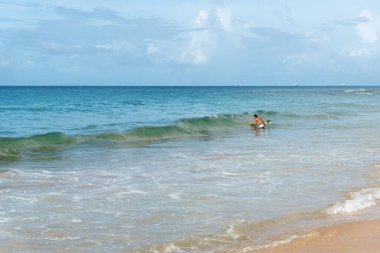 A surfer entering the sea against blue sky and white clouds. Salvador, Brazil.