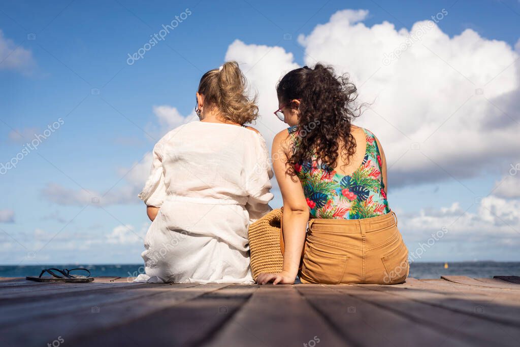 Mother and daughter sitting on the pier of the port of Barra facing the sea. Salvador, Bahia, Brazil.