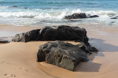 A wave breaks about a rock during a curtain on the sea. Farol da Barra beach, Salvador, Brazil.