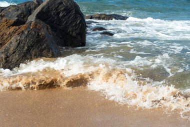 A wave breaks about a rock during a curtain on the sea. Farol da Barra beach, Salvador, Brazil.