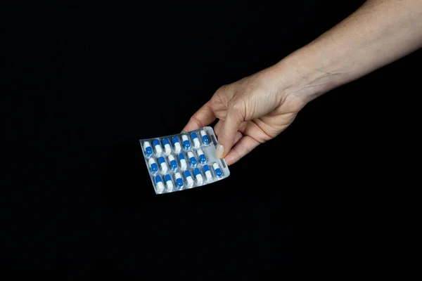 A hand holds pill packs of assorted colors against a black background. Medical material.