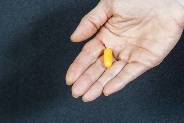 A yellow pill in the palm of a hand against a black background. Medical material.