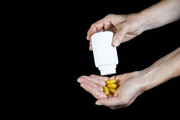 One hand pours yellow pills into the palm of another hand against a black background. Medical material.