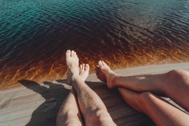 Legs of a man and a woman by the river against reddish water in the background. Guaibim beach in the city of Valenca, Bahia, Brazil.
