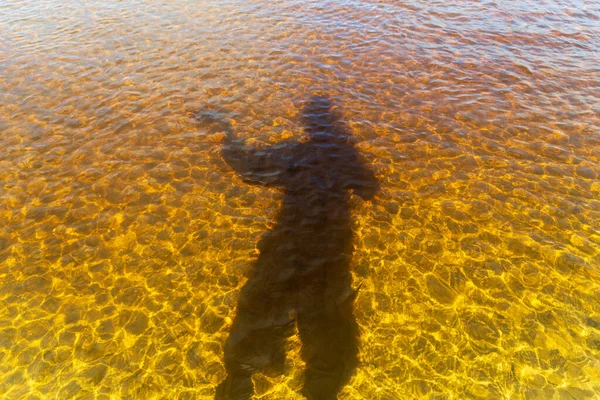 Shadow of a man wearing a hat, in the water of the Guaibimzinho River. Praia do Guaibim, coast of the sea of Bahia, Brazil