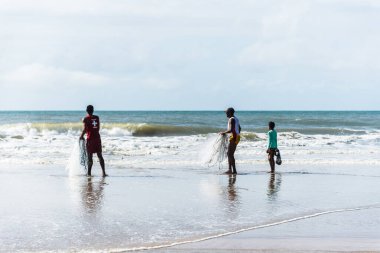 Fishermen are seen walking on the beach against the sea and the blue sky in the background. Guaibim beach in the city of Valenca, Bahia, Brazil.