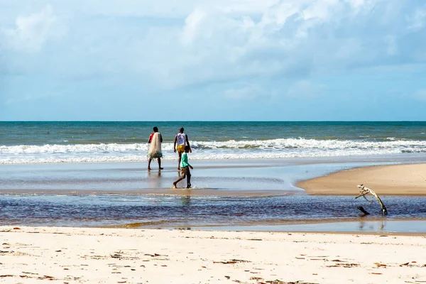 Fishermen are seen walking on the beach against the sea and the blue sky in the background. Guaibim beach in the city of Valenca, Bahia, Brazil.