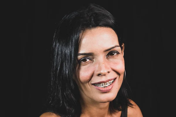 Studio portrait of young woman in black t-shirt smiling at camera against black studio background. Salvador, Brazil.