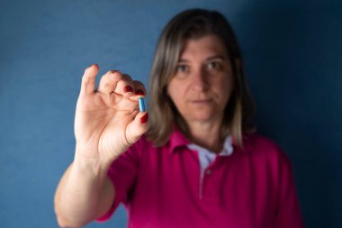A woman holds a blue pill in her hand against a blue background. Medical supplies.