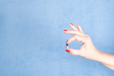Pill held by the fingers of a hand against blue background. Medical supplies.