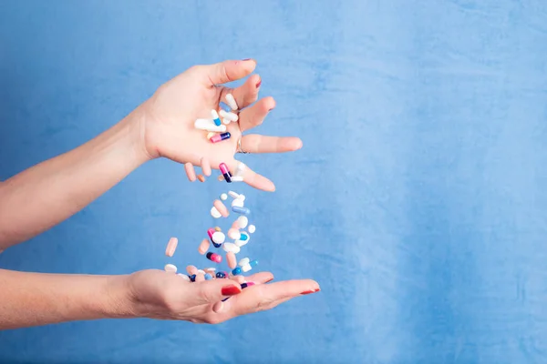Several pills falling from one hand to another against blue background. Medical supplies.
