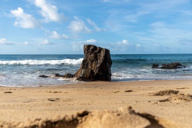 A wave breaks about a rock during a curtain on the sea. Farol da Barra beach, Salvador, Brazil.