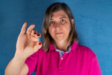 A woman holds a blue pill in her hand against a blue background. Medical supplies.
