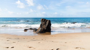 A wave breaks about a rock during a curtain on the sea. Farol da Barra beach, Salvador, Brazil.