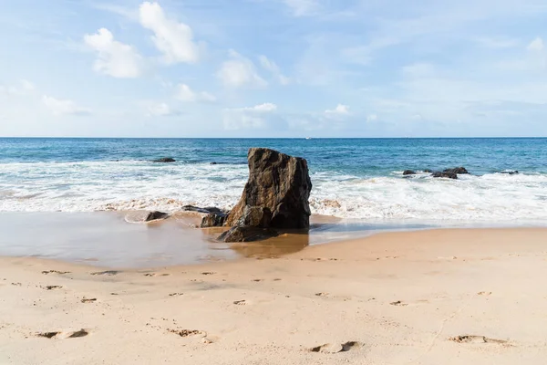 A wave breaks about a rock during a curtain on the sea. Farol da Barra beach, Salvador, Brazil.