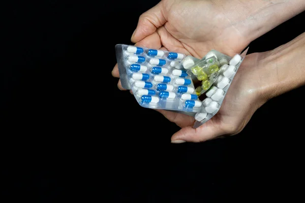 Hands hold pill packs of assorted colors against a black background. Medical material.