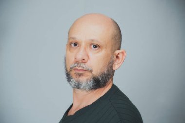Portrait of mature man standing on white background. Bald bearded man looks at the camera. Formal style.