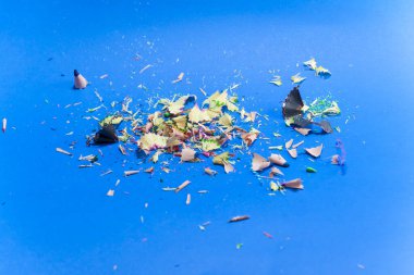 Mavi arka planda izole edilmiş renkli kalemlerin kalıntıları. Kapatın. Keskinleştirilmiş kalem artıkları.