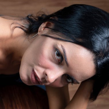 Studio portrait of young woman in black t-shirt looking at camera against wooden floor on floor. Salvador, Brazil.