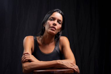 Studio portrait of young woman looking at camera against simple studio black background. She wears a black t-shirt.