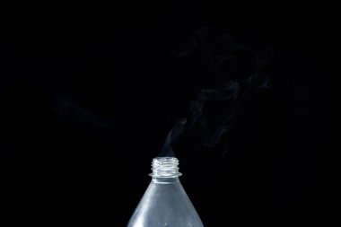 Plastik bir şişeden siyah bir arka planda duman çıkıyor. Cadılar Bayramı için arka plan. Doku sisi. Tasarım elemanı. Aromaterapi kavramı.