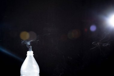 Plastik şişeden çıkan duman siyah arka planda parlıyor. Cadılar Bayramı için arka plan. Doku sisi. Tasarım ögesi.