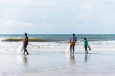 Fishermen are seen walking on the beach against the sea and the blue sky in the background. Guaibim beach in the city of Valenca, Bahia, Brazil.