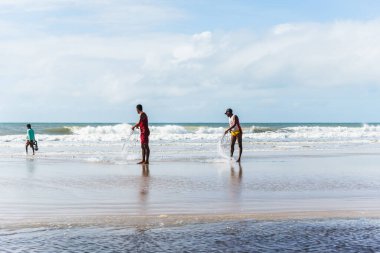 Fishermen are seen walking on the beach against the sea and the blue sky in the background. Guaibim beach in the city of Valenca, Bahia, Brazil.