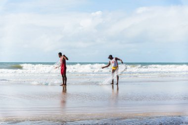 Fishermen are seen walking on the beach against the sea and the blue sky in the background. Guaibim beach in the city of Valenca, Bahia, Brazil.