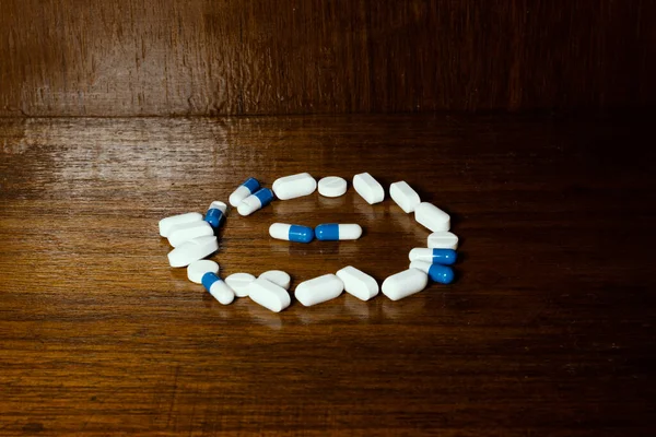 Simple pile of white and blue pills, medicines, pills stacked on brown background. Medical supplies.