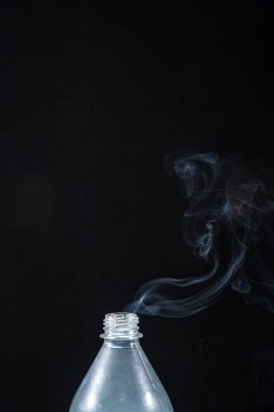 Plastik bir şişeden siyah bir arka planda duman çıkıyor. Cadılar Bayramı için arka plan. Doku sisi. Tasarım elemanı. Aromaterapi kavramı.