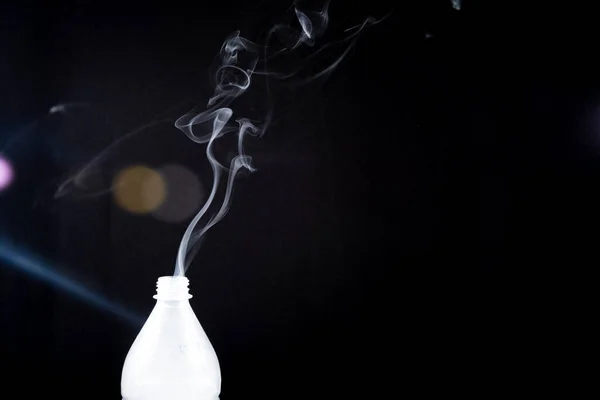 Smoke coming out of a plastic bottle against a black background with flare. Background for Halloween. Texture fog. Design element.