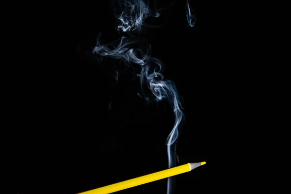 A yellow colored pencil touching the white smoke coming from below. Close up. Sharp pencil scraps.
