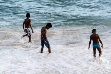 Salvador, Bahia, Brezilya - 1 Nisan 2018: Brezilya 'nın Salvador kentindeki Farol plajında üç genç atlama oyunu oynuyor. Bulutlu ve güzel bir gün.