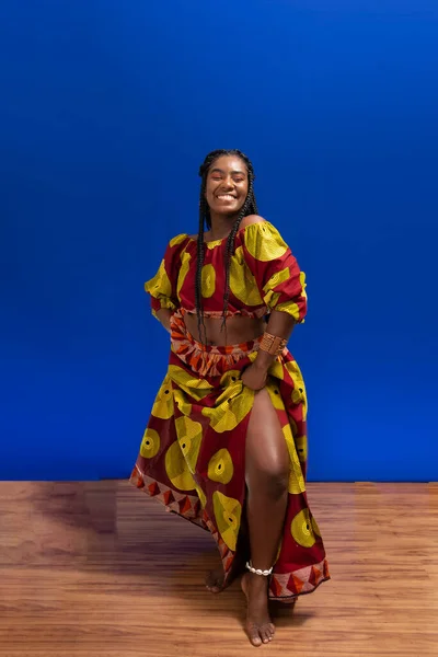 Afro-Brazilian woman dressed in African style standing against blue background. Happy and confident young man.